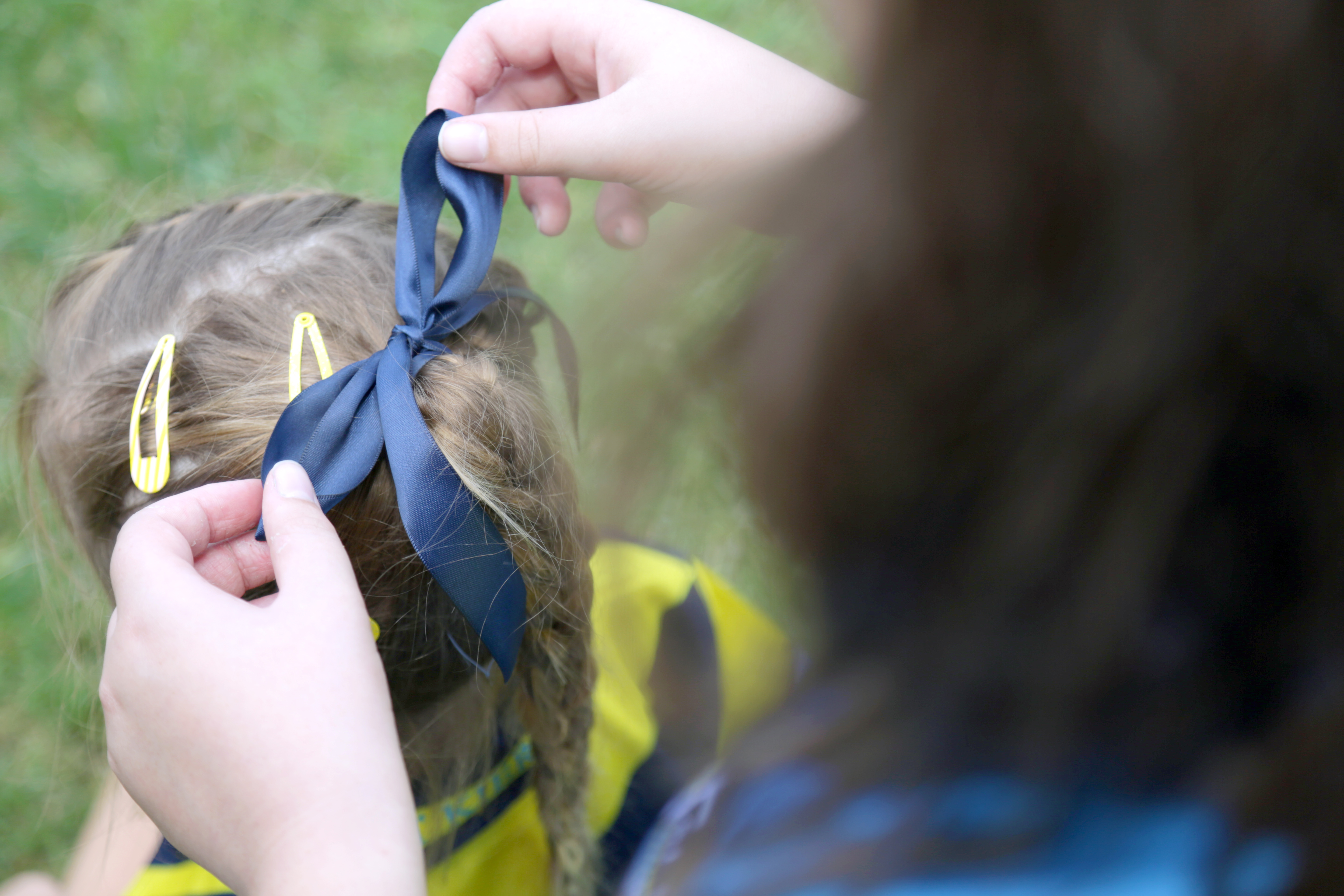Child having a ribbon tied into their hair by an adult outdoors